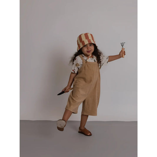 Kind mit tanfarbenen Cord-Latzhose und gestreiftem Eimerhut