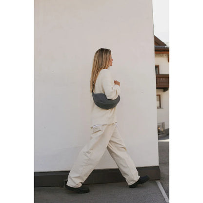 Frau in cremefarbenem Pullover und passender Hose mit grauer Crescent-Umhängetasche