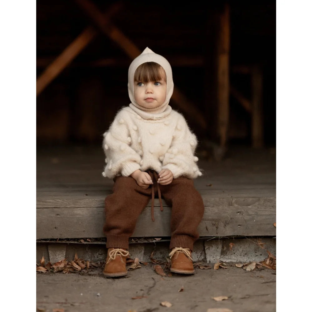 Kleiner Junge in cremiger Bobbelstrickjacke, braunen Hosen und Balaclava mit Desert Winter Boot Chestnut
