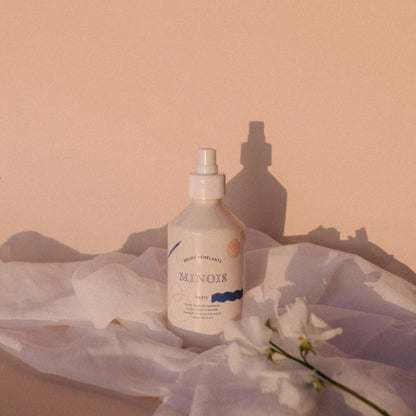 Ein weißes sleekes sprayfläschchen mit minimalistischem label von munos paris und abstrakten blauen und orangen akzenten auf weichem stoff für entwirrungsspray 300 ml