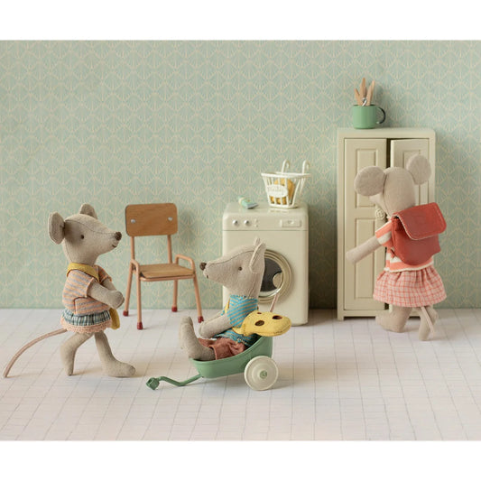 Eine weiche beige plüschmaus namens dreirad-maus grosse schwester in kleid und gelben trägern neben grünem spielwagen, nachhaltige babykleidung schweiz
