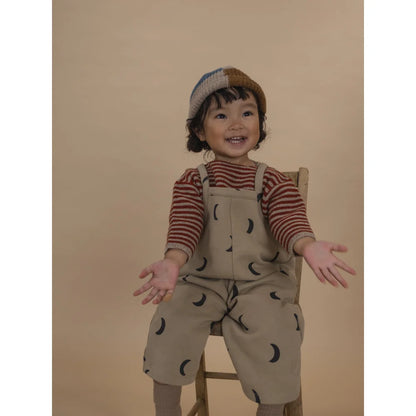 Lächelndes Kind in gestreiftem Hemd, Mond-überzogene Latzhose und Farbblock-Strickmütze