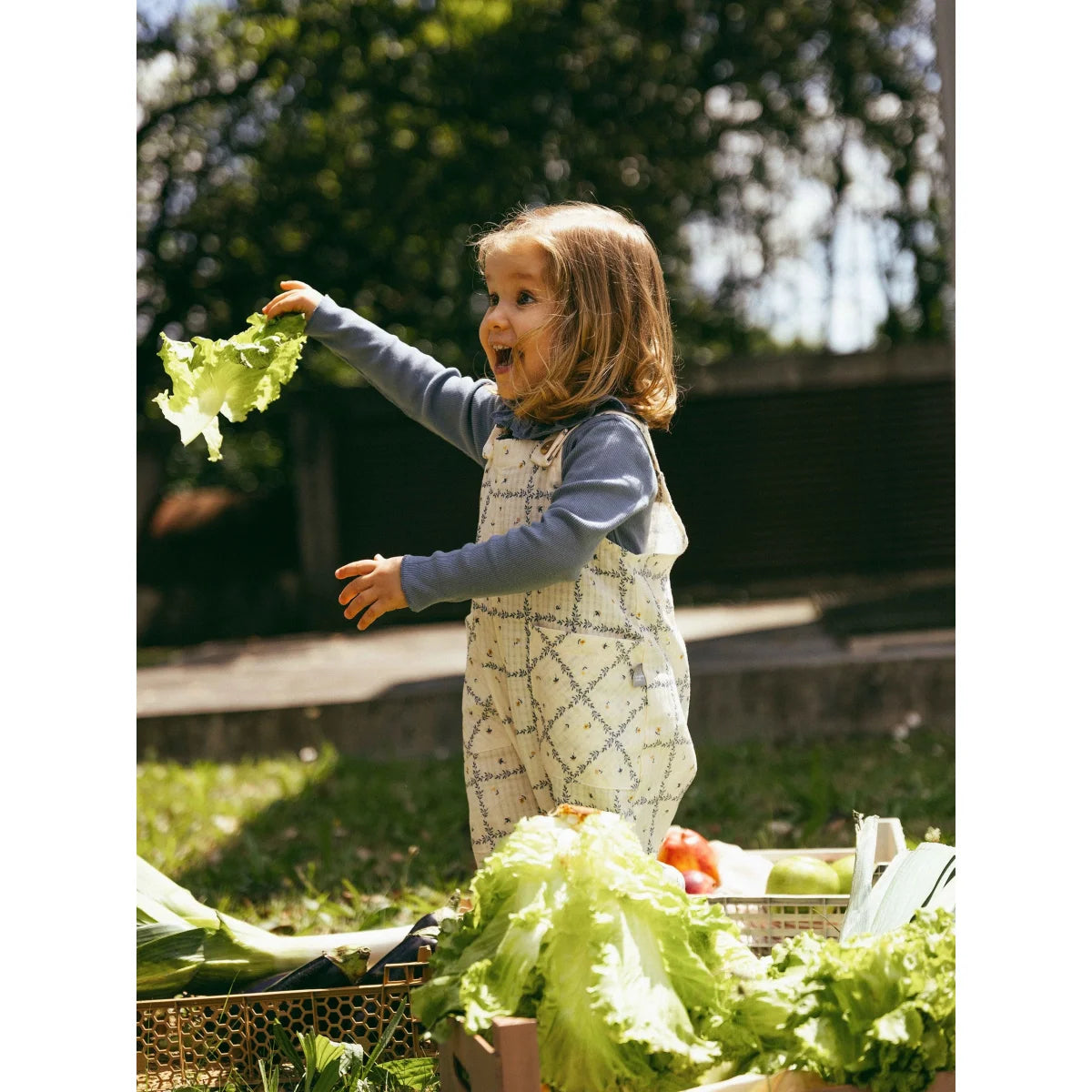 Fröhliches Kind in gestreiftem Dungarees Indigo mit Salatblatt