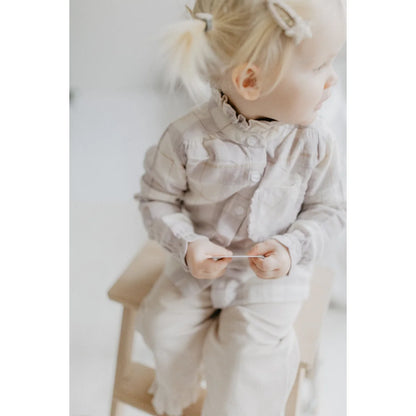 Junges Kind in beiger und lavendelfarbener Flanellbluse mit Rüschenkragen, hält kleinen Gegenstand