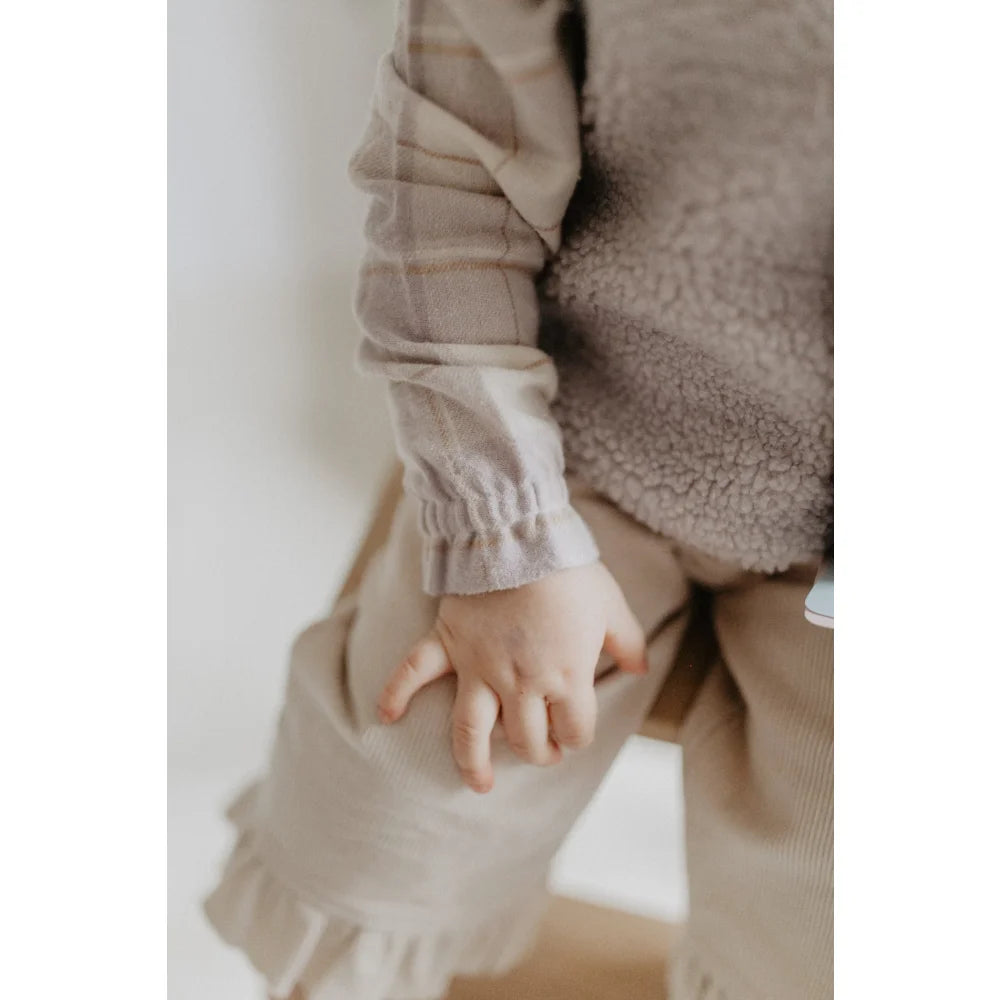 Kinderhand auf hellfarbiger, geraffter Hose bei Flanellbluse beige lavender