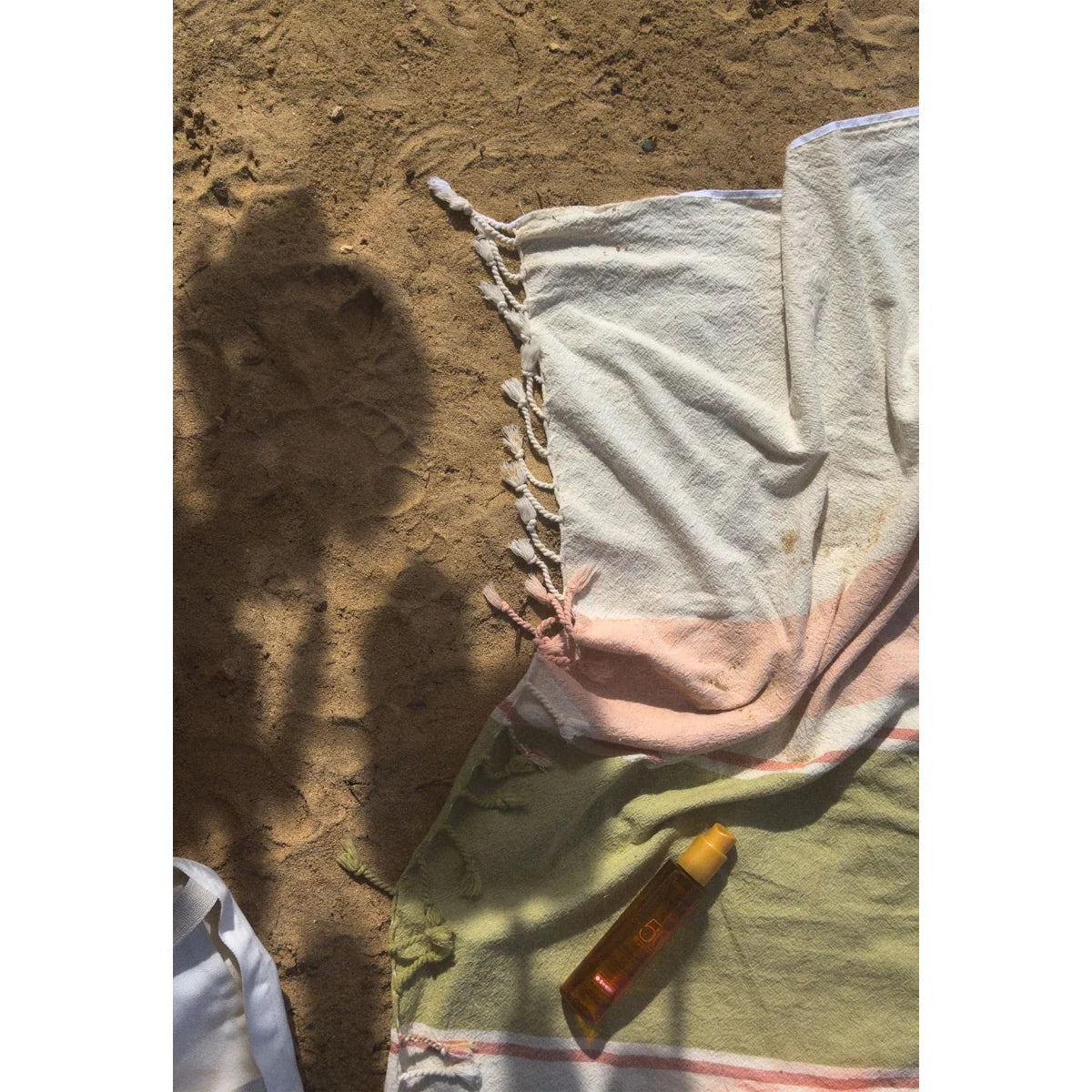 Ein golden-orangefarbener sonnenlotion-flakon mit gelbem deckel auf einem gestreiften fouta baumwolltuch sea für ökologische baby- und kinderprodukte