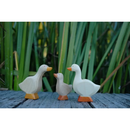 Drei hölzerne Gänsefiguren mit orangefarbenem Schnabel und Füßen