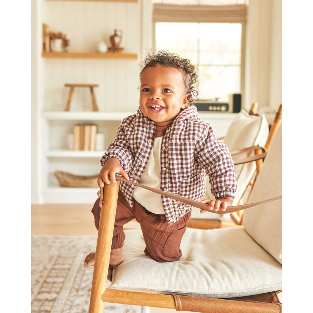 Smiling toddler in plaid shirt and brown pants kneeling on a chair with Gewebte Jacke