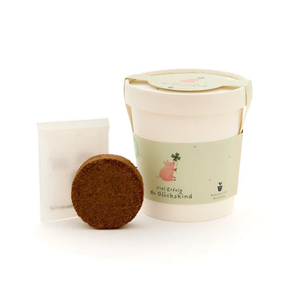 Ein cremefarbener keramiktopf glückskind becher mit grünem band und rosa schwein illustration für ökologische baby- & kinderprodukte