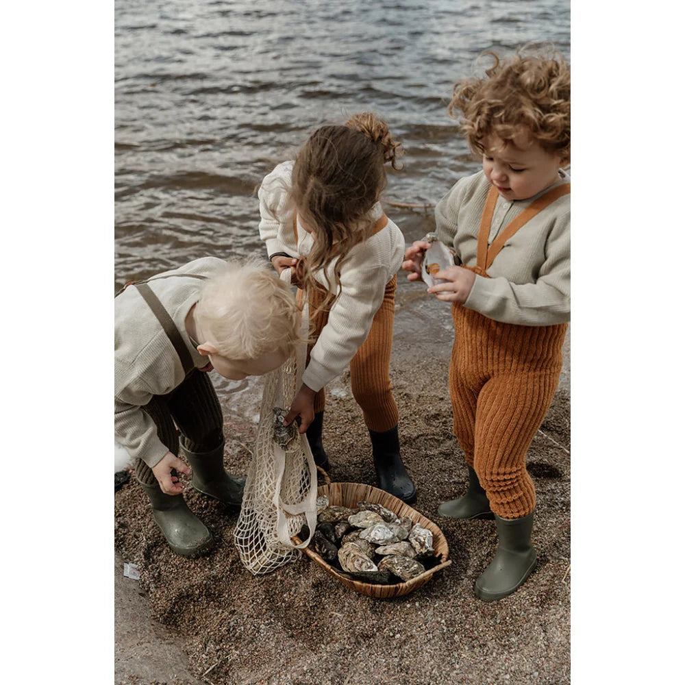 Drei Kinder erkunden eine felsige Küstenlinie und sammeln Gegenstände