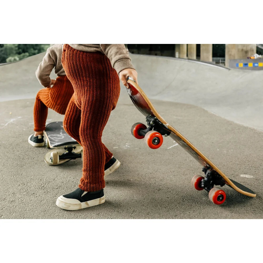 Skateboard mit leuchtend orangefarbenen Rollen in Händen einer Person in rustfarbenen Hosen