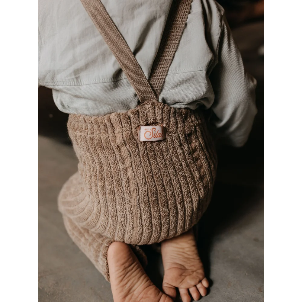 Beiger Corduroy Baby-Romper mit Trägern und sichtbaren nackten Füßen im Peanut Blend