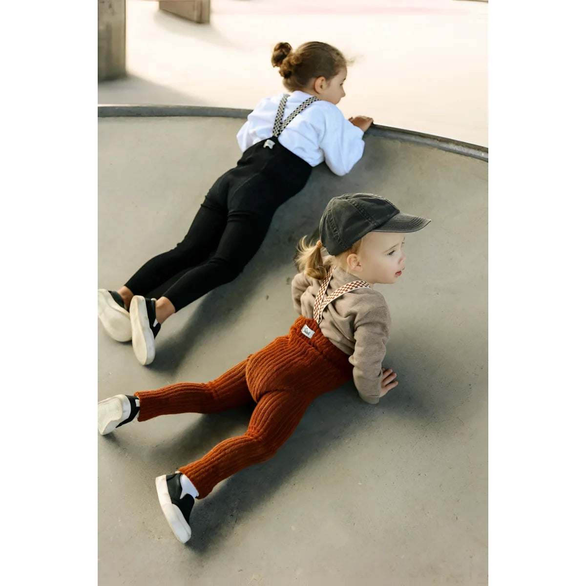 Zwei Kinder liegen bäuchlings in einer Skatebowl, das vordere in zimtfarbener Granny Teddy Strumpfhose mit karierten Trägern