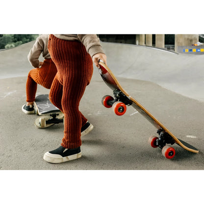 Kind mit Skateboard im Skatepark, in zimtfarbener Granny Teddy Strumpfhose im breiten Rippstrick