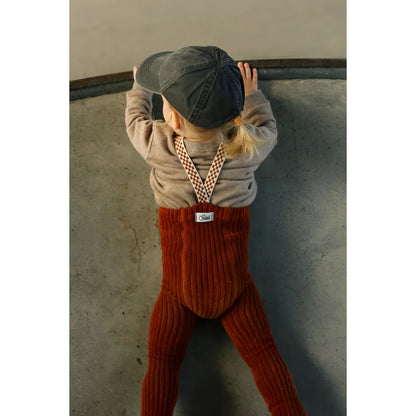 Kind von oben fotografiert in zimtfarbener Granny Teddy Strumpfhose, die karierten Träger liegen über dem Pullover