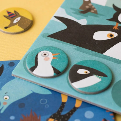 Runde Holzspielmarken mit Pinguin- und Haifisch-Motiven auf türkisem Grund für Habitats Lotto