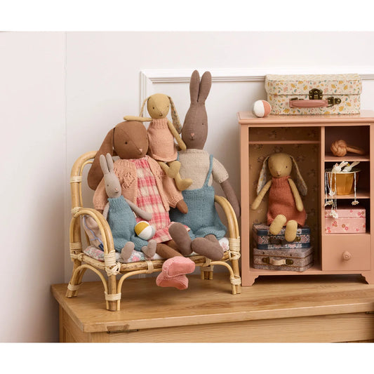 Eine gemütliche sammlung weicher pastellfarbener stoffhasen in gestrickten cremegelben outfits auf einem rattanbank