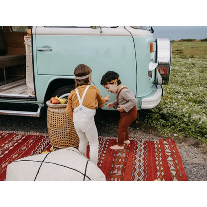 Zwei Kinder in Erdfarbenoutfits bei blau-weißem VW-Bus, mit Trägern und Zimt