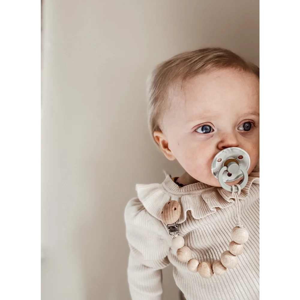 Baby mit großen Augen, Schnuller und Rüschenshirt, Holz Nuggikette in Honigfarbe