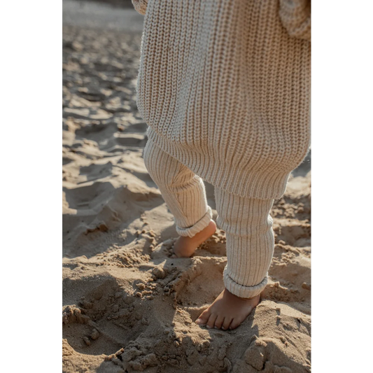 Barfuß auf einem Sandstrand mit lockerer, cremefarbener Strickhose