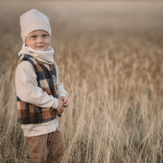 Kind im Winterkleidung steht in einem Feld mit Karo Weste