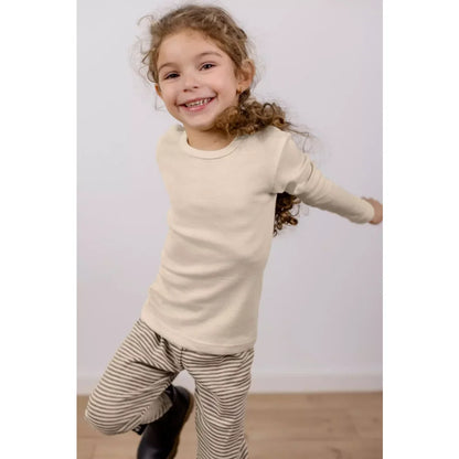 Junges Mädchen trägt langärmliges cremefarbenes Oberteil und gestreifte Hosen