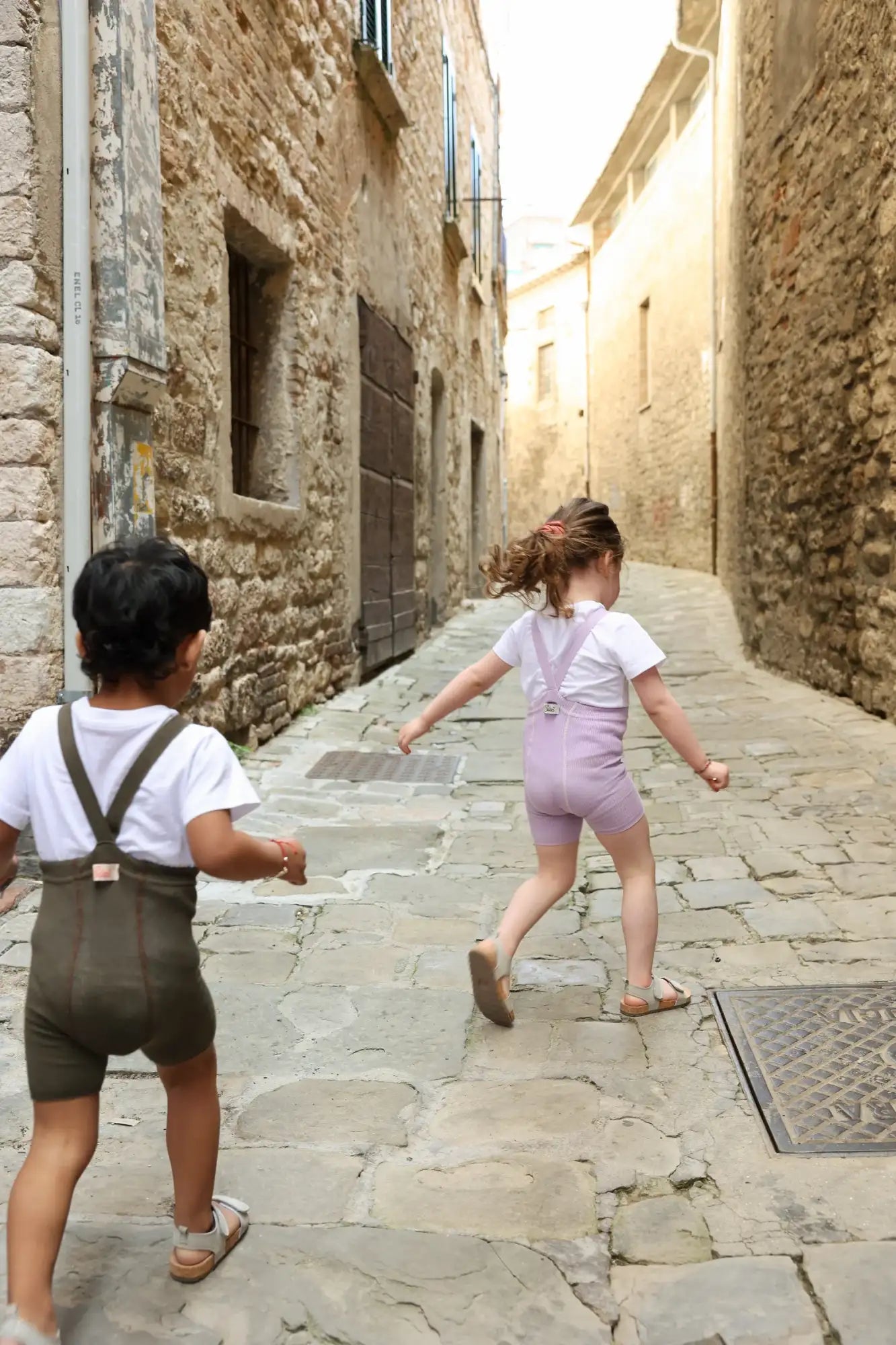 Die Kinder tragen passende Overalls in Olivgrün und Lavendel mit verstellbaren Trägern, kombiniert mit weißen T-Shirts.