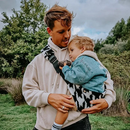 Mann hält ein Kind im Freien in der Kindertrage Houndstooth Teddy