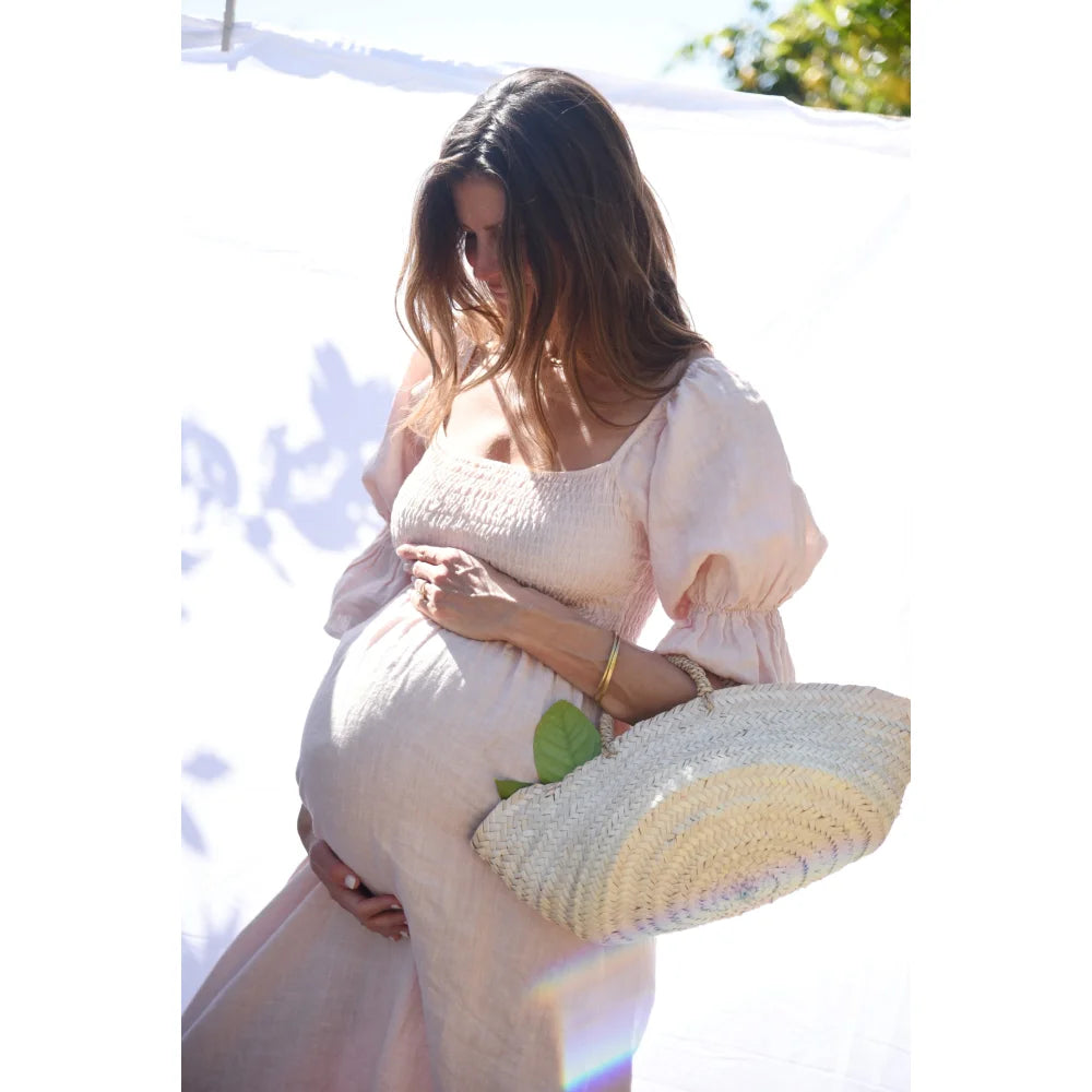 Schwangere Frau in weißem Kleid mit Strohtasche, Modell Kleid Deia in Blush