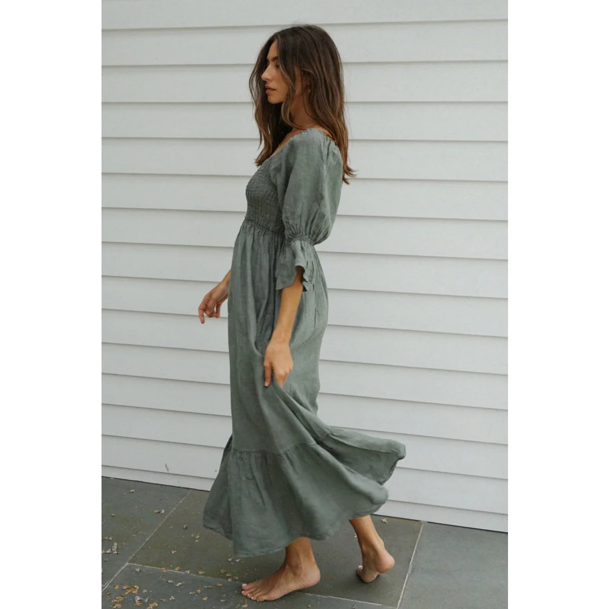 Ein fließendes maxikleid deia in salbeigrün aus leinen mit smock-bustier und stufenhaftem saum ideal für ökologische baby- und kinderprodukte
