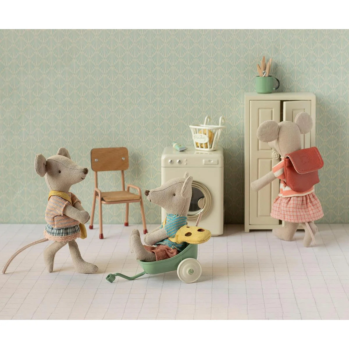 Eine weiche beige mausfigur mit blauem pullover und brauner hose sitzt in einem mintgrünen spielzeugwagen kleine schwester mit tasche