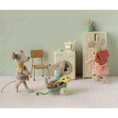 Eine weiche beige mausfigur mit blauem pullover und brauner hose sitzt in einem mintgrünen spielzeugwagen kleine schwester mit tasche