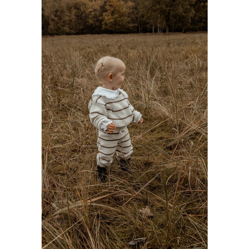 Kleinkind in gestreiftem Outfit steht auf einem Feld mit hohem Gras