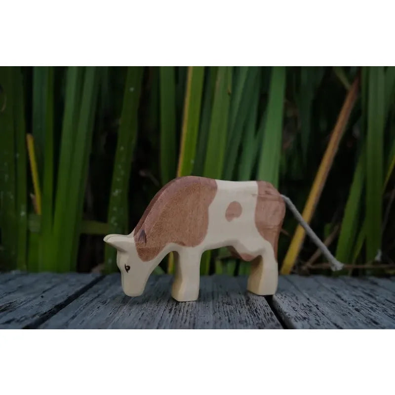 Handgeschnitzte Holzspielzeugkuh mit braunen und cremefarbenen Flecken, Kuh fressend