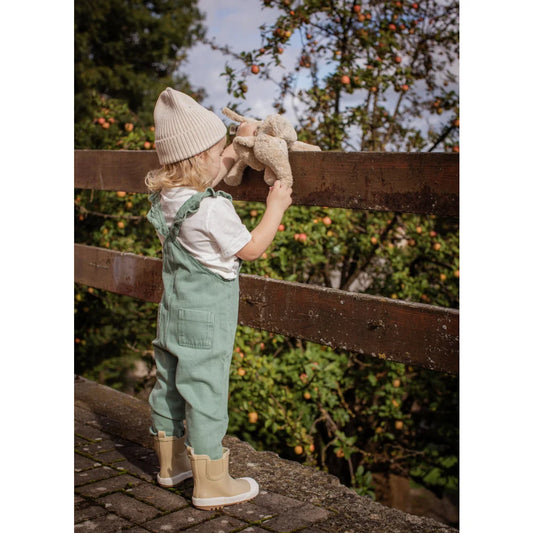 Kind mit minzgrünen Latzhose und beigem Strickmützchen