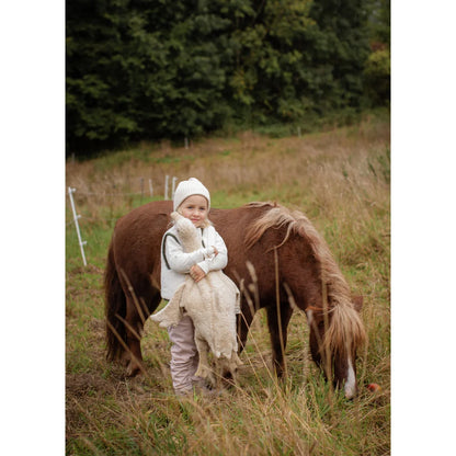 Kleines Kind mit weißer Strickmütze bei braunem Pony und Gans-Kuscheltier