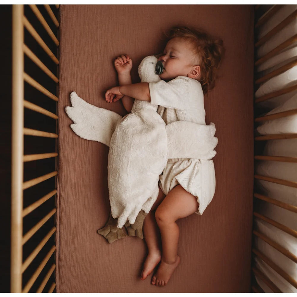 Schlafendes Baby in einem weißen Engelkostüm in einem Kinderbett mit Kuscheltier Gans