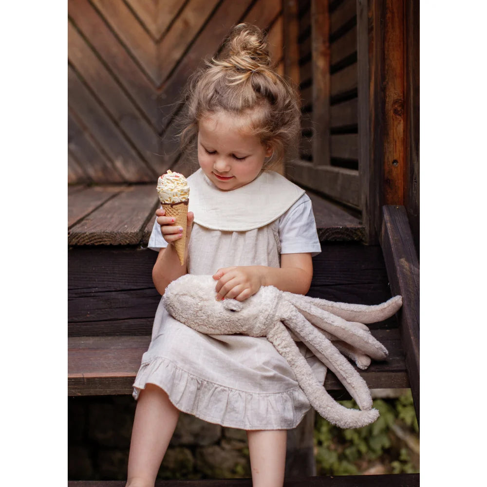 Kleines Mädchen in hellem Kleid hält Vanille-Eis mit Streuseln, Kuscheltier Oktopus puder klein