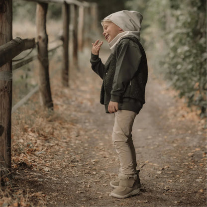 Junges Kind in lockeren hellbeigen Hosen, bequemer Mütze und dunklem Parka