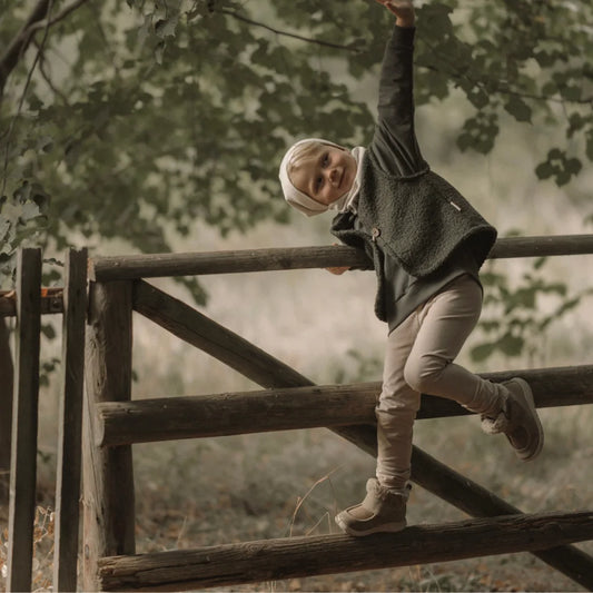 Ein junges Kind in gemütlicher Kleidung klettert einen Holzzaun hinauf