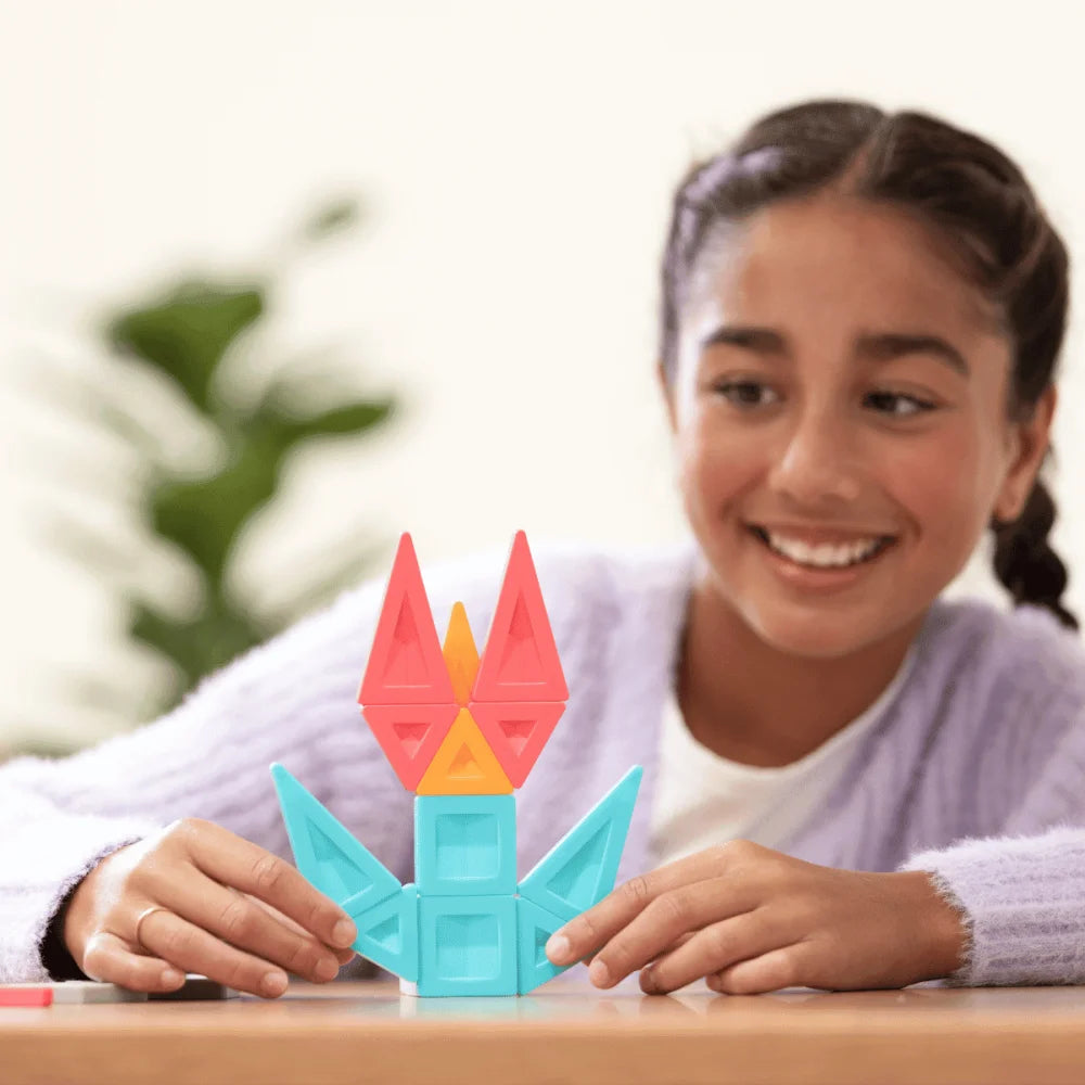 Lächelndes Mädchen mit dunklen Zöpfen und lila Cardigan spielt mit bunten Magnetbausteinen