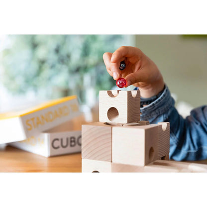 Hand hält transparente rote Cuboro Kugel über Holzbausteinen