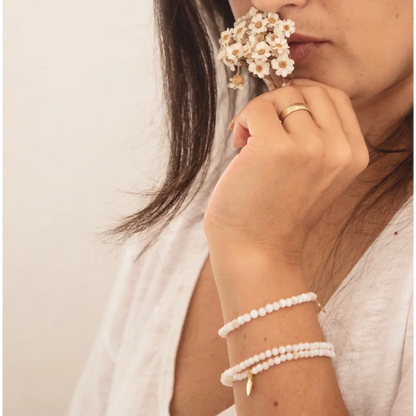 Perlenarmbänder am Handgelenk, goldener Ring und weiße Blumen nahe dem Gesicht