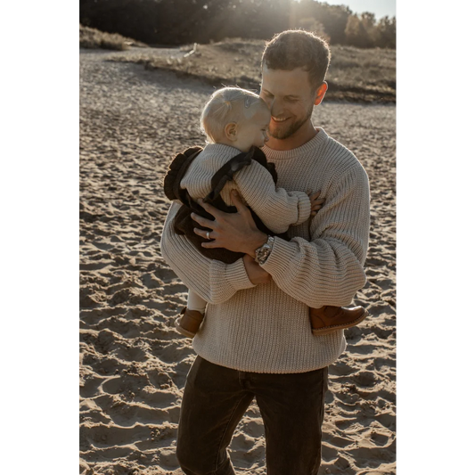 Mann hält ein Baby am Strand in einem chunky Strickpullover in Oat