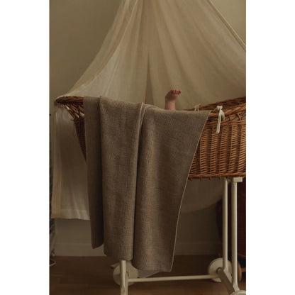 Wicker bassinet with gray blanket and white canopy showcasing Merino Strickdecke Ivy Pebble