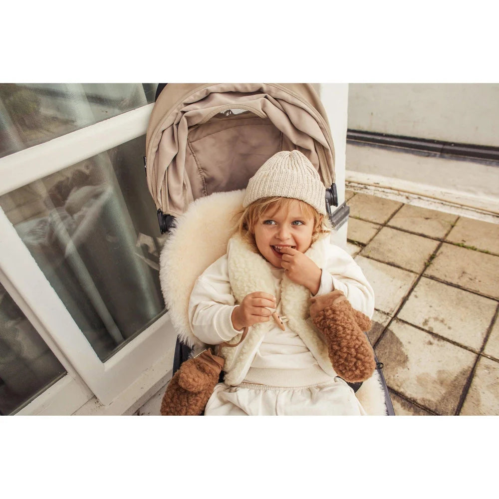 Junger Kind im Kinderwagen mit Merino Weste Milk und Strickmütze in Weiß