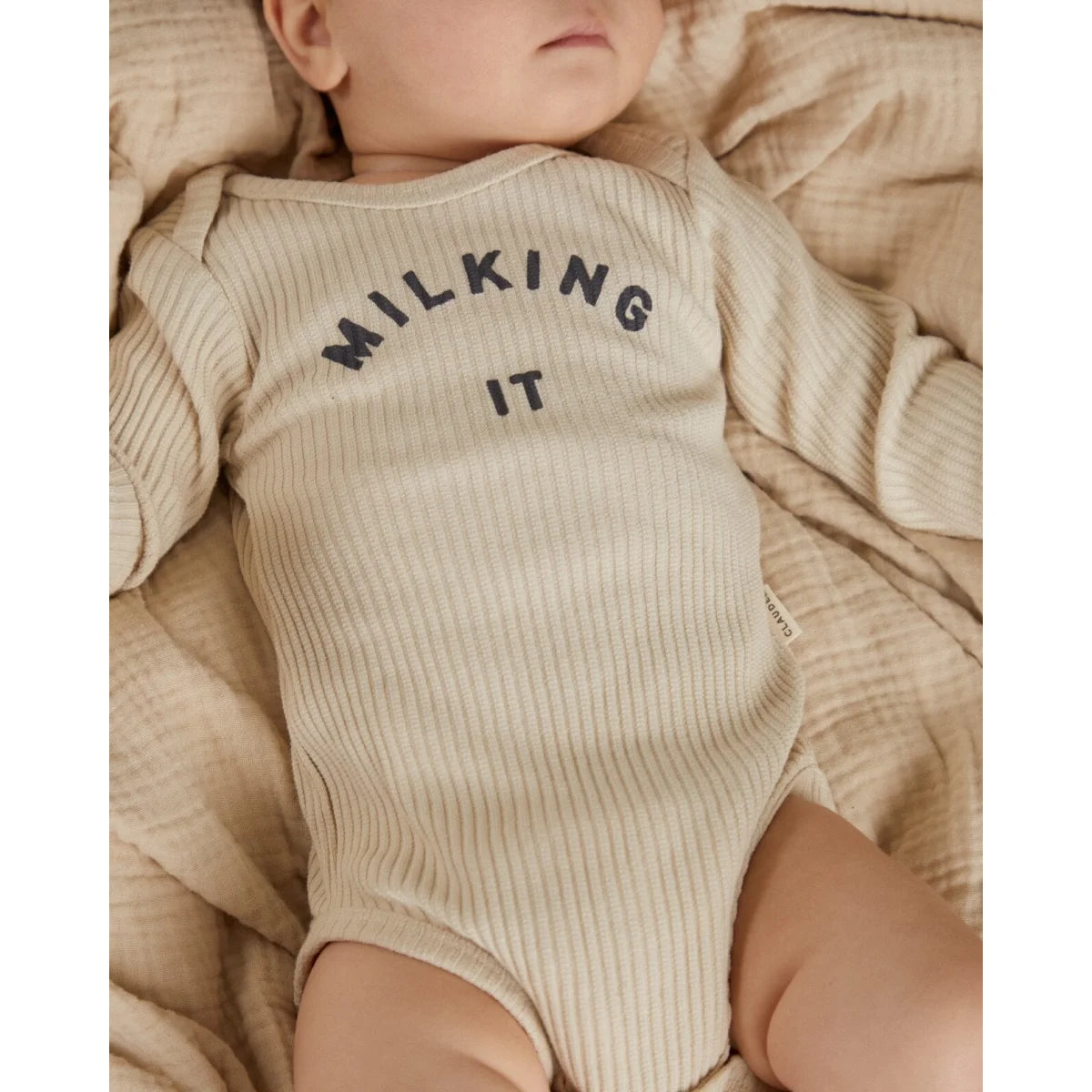 Beige geripptes langarm babystrampler aus baumwolle mit dunkler grauer aufschrift milking it bodesuit oat