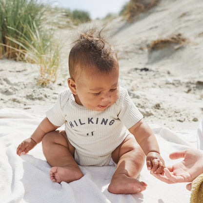 Baby in einem creamfarbenen gerippten kurzarm-bodysuit milking it aus der collection oat von milking it