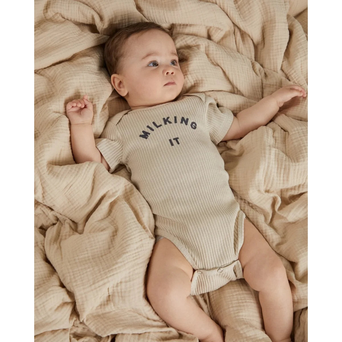 Ein weiches geripptes beige baby-strampler kurzarm mit dem aufdruck milking it in dunkelgrau auf der brust