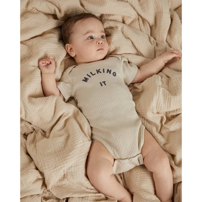 Ein weiches geripptes beige baby-strampler kurzarm mit dem aufdruck milking it in dunkelgrau auf der brust